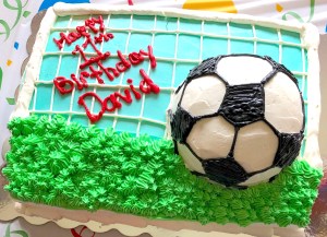 Photo of a soccer field shaped birthday cake with an edible soccer ball on the top